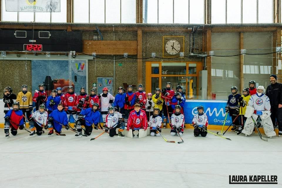 Große Gruppe junger Eishockeyspieler:innen mit Trainern in der Eishalle